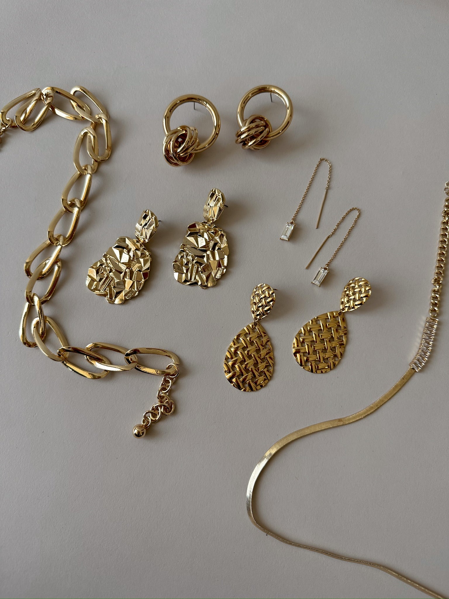 gold earrings, gold hoops, 2 gold necklaces laid out flat on grey paper