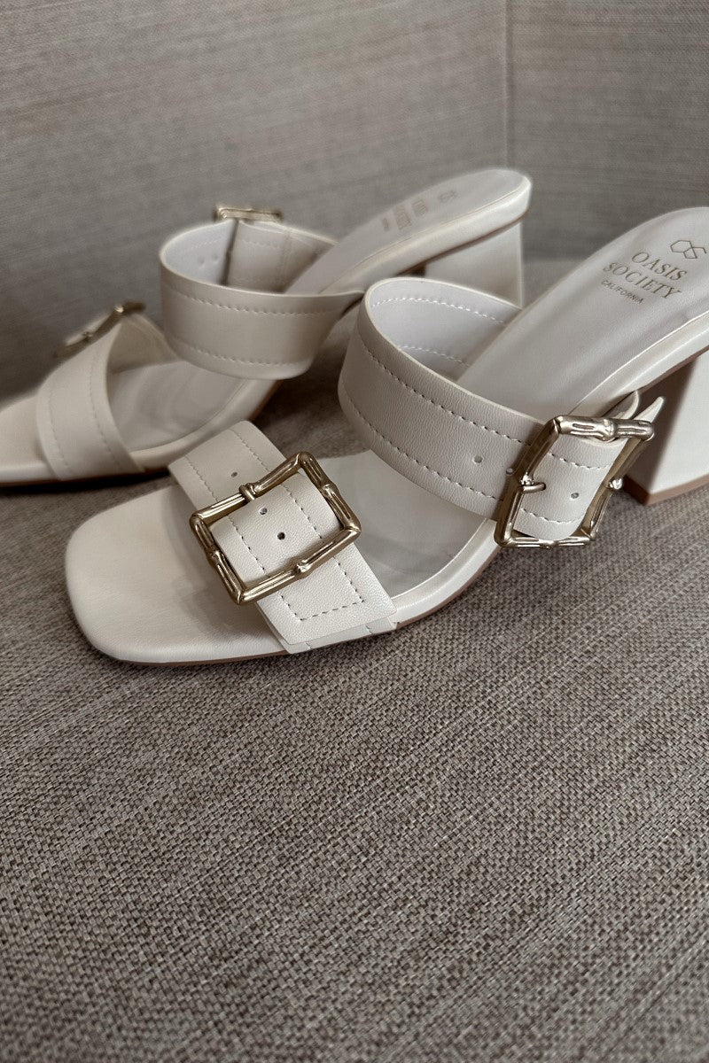 Close side view of the Havana Beige Heeled Sandals that feature beige faux-leather material, two straps with adjustable gold buckles, square toes, and 2.5" block heels.
