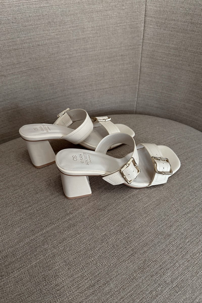 Side view of the Havana Beige Heeled Sandals that feature beige faux-leather material, two straps with adjustable gold buckles, square toes, and 2.5" block heels.
