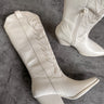 Aerial view of the Sierra Cream Western Boots that feature cream faux-leather with monochromatic western stitching, inner zipper closures, pointed toes, and 2.5" cream heels.