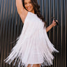 Side view of model wearing the Karissa White Fringe Tiered Mini Dress which features white fringe fabric, white lining, mini length, halter neckline with button closure, sleeveless and open back.