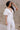 Side view of model wearing the Bella Ivory Plunge Neckline Flare Jumpsuit which features white knit fabric, plunge neckline, short flare sleeves, open back, monochrome back zipper with hook closure and flare pant legs.