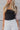 Close up view of model wearing the Luna Black Sleeveless Bodysuit which features black knit fabric, a square neckline with a racerback, a sleeveless body, and a thong bottom with snap closures.