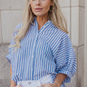 Front view of model wearing the Ella Blue & White Stripe Button Up Top which features dark blue and white fabric with a striped pattern, white button-up front closures, an oversized fit, a collared neckline and short sleeves with cuffs.
