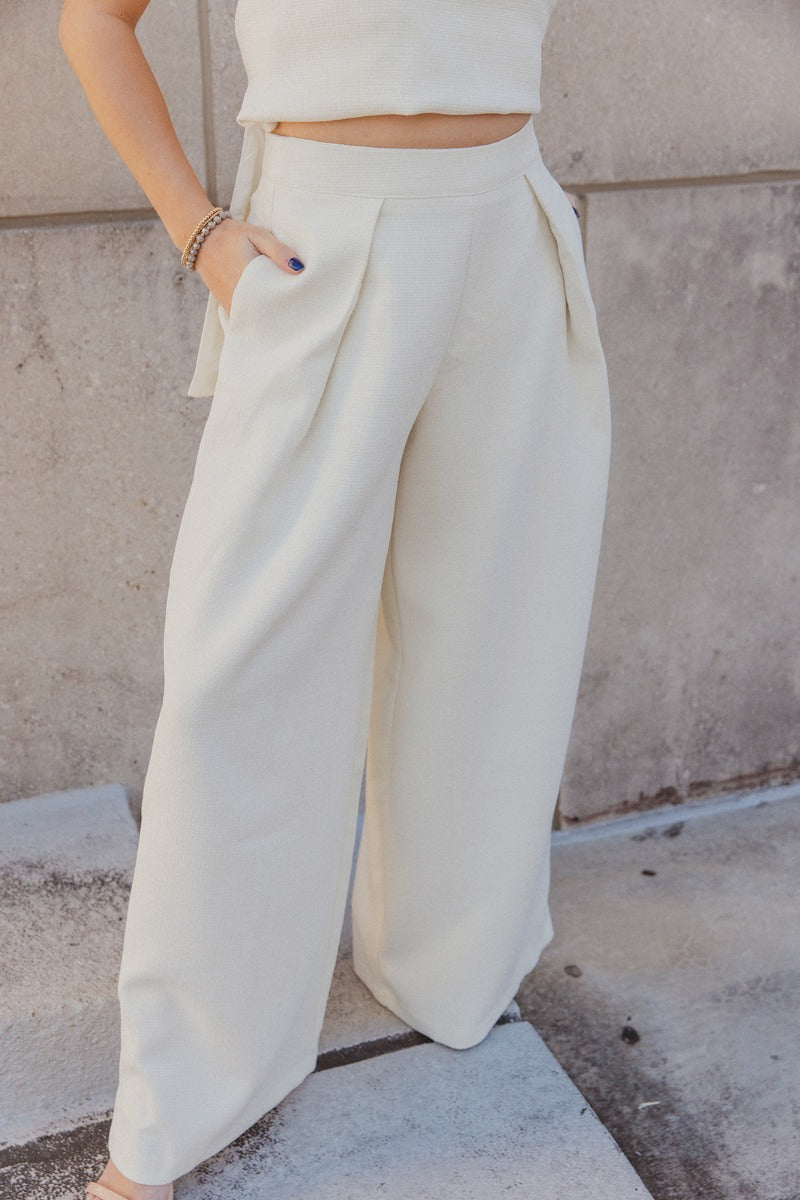 Front view of model wearing the Grace Ivory Wide Leg Pants which features ivory textured fabric, two side slit pockets, monochrome side pockets, and wide pant legs.