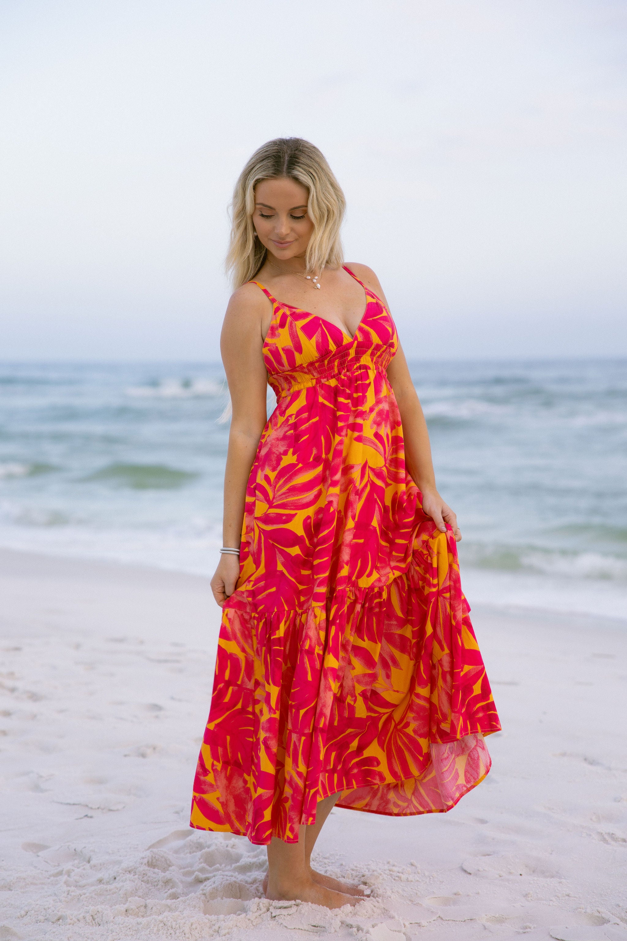 Full body front view of female model wearing the Melina Orange & Pink Floral Maxi Dress that has bright orange and pink floral pattern, adjustable straps, and an open back.