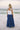Full body back view of female model wearing the Madelyn White Tie Strap Tank Top that has tiered white fabric and tie straps with navy trim. Worn with blue skirt.