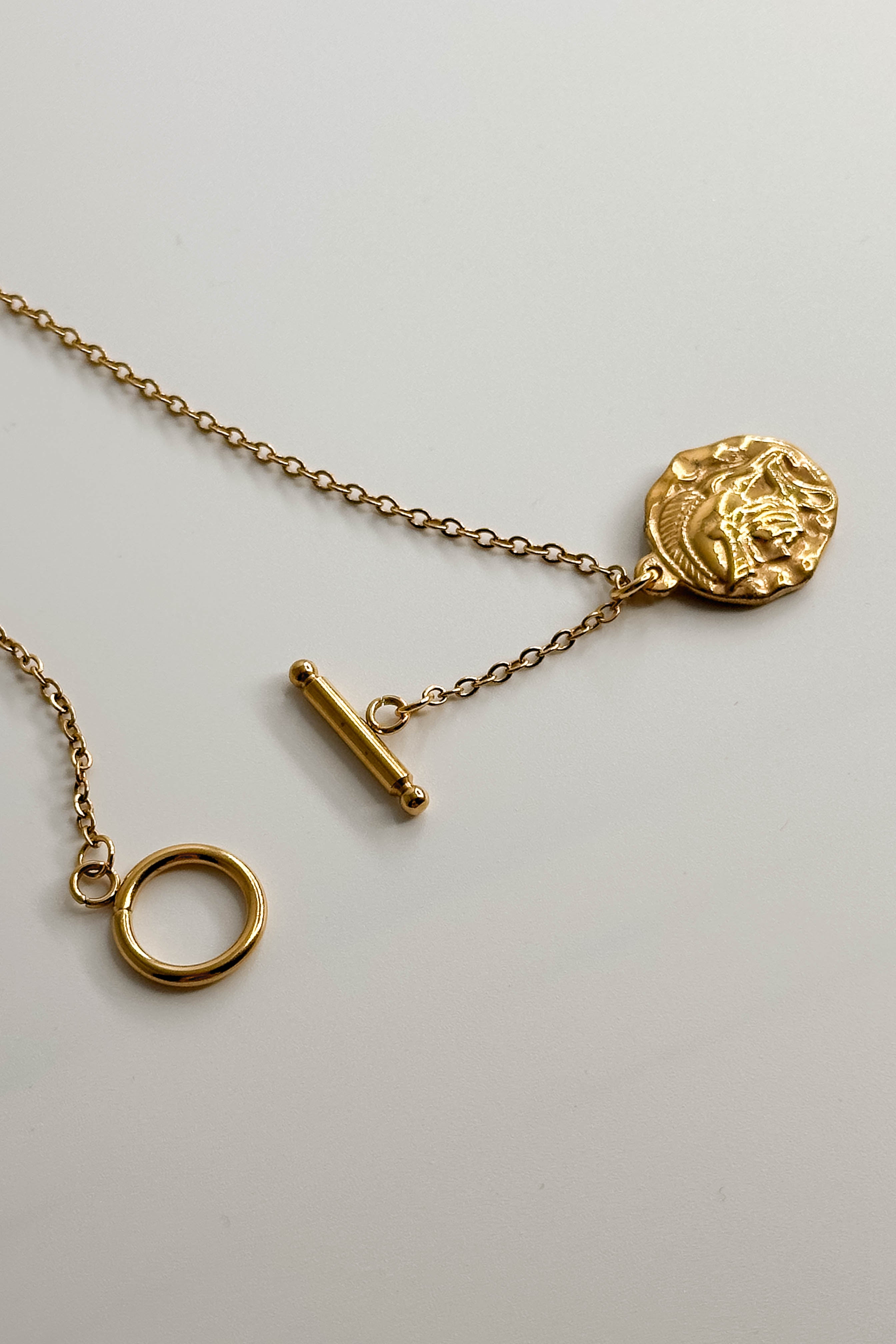 Close-up image of the Alexandra Gold Medallion Necklace against a white background. Necklace has gold chain with toggle closure and gold circle medallion with side profile of a gladiator. Necklace is shown unhooked