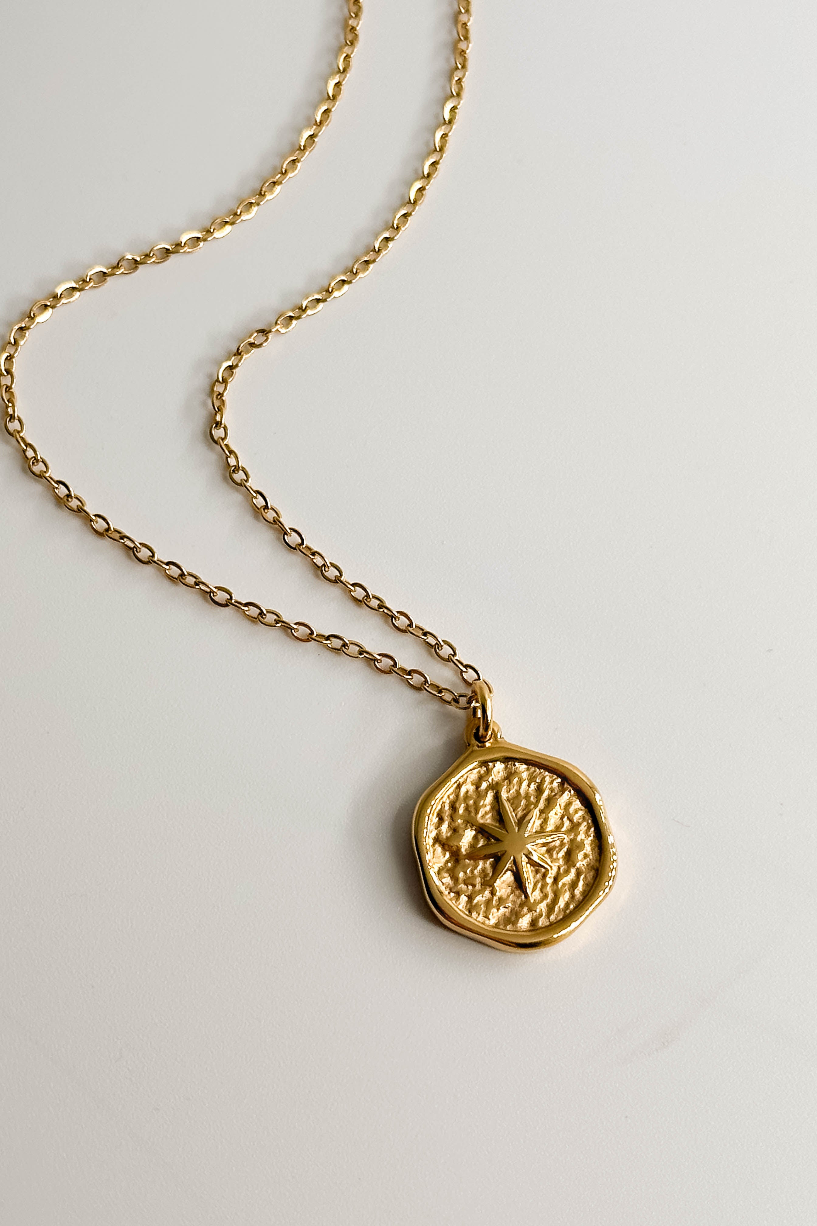 Image shows close-up of the Celeste Gold Star Medallion Necklace against a white background. Necklace has gold chain with circle medallion which has an 8 point star in the center.