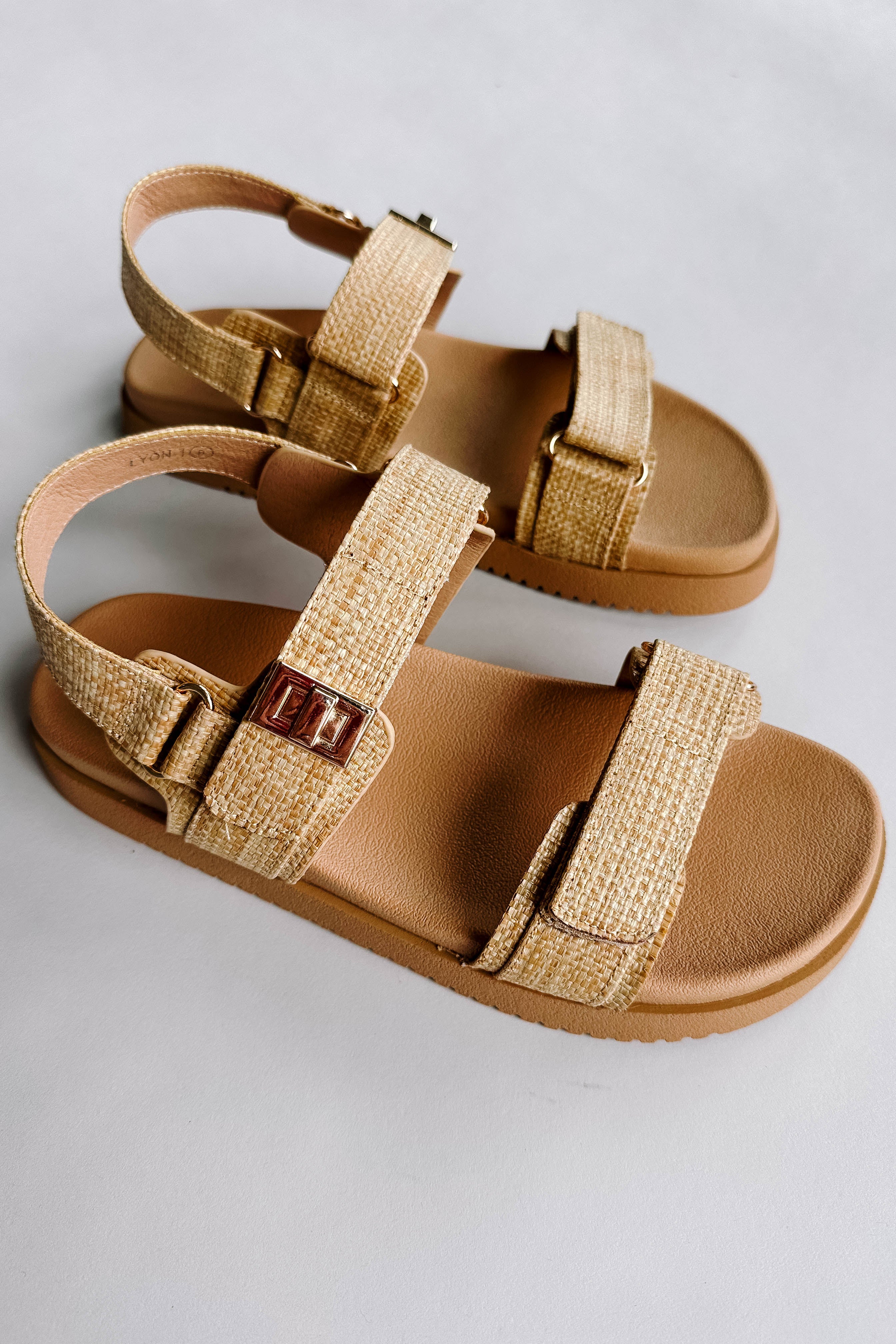 Side view of the Lyon Sandal in Beige Raffia which features natural raffia fabric, two adjustable velcro straps, adjustable back strap and round toe.