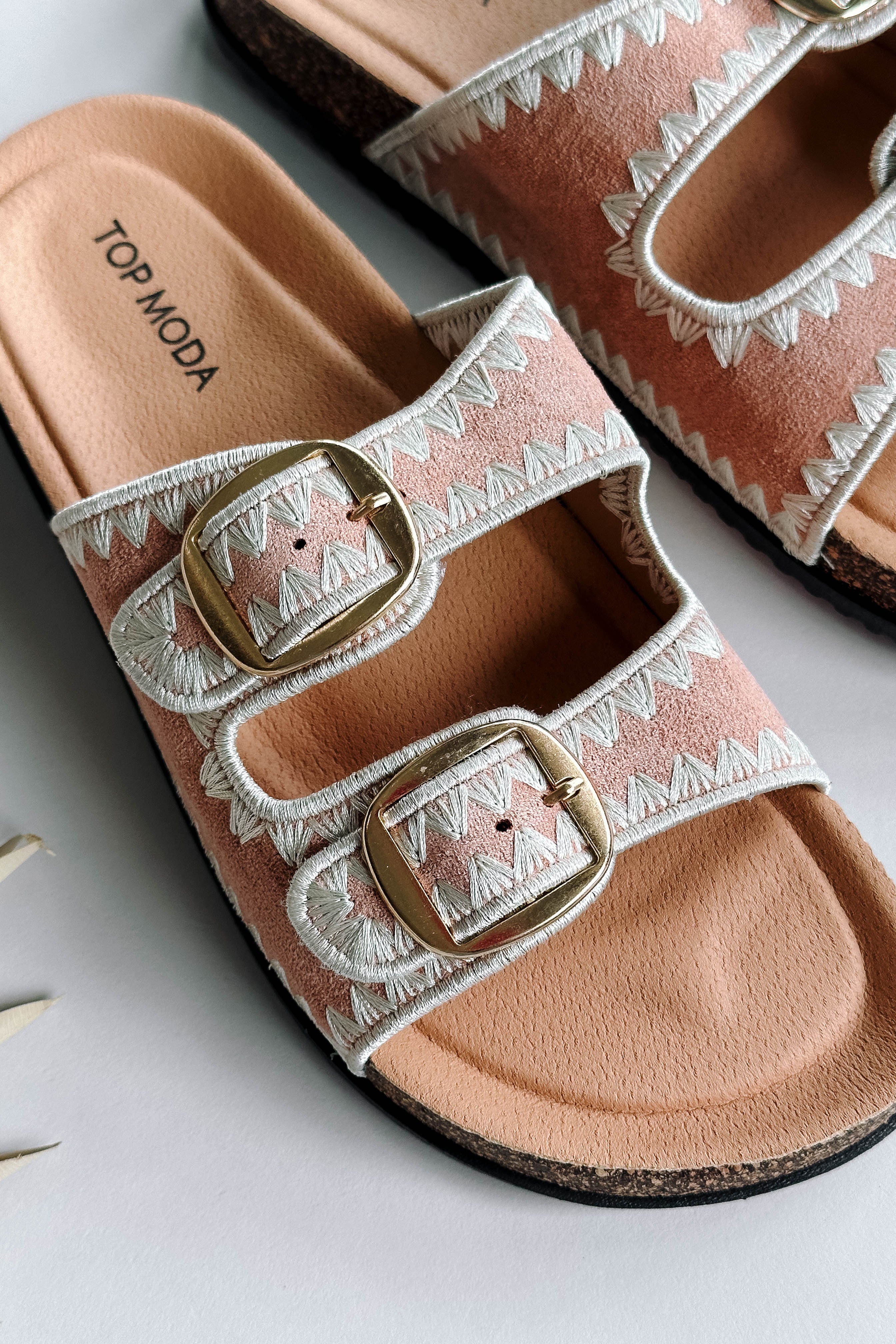Close up view of the Luca Sandal in Blush which features blush fabric, cream geometric trim design, two adjustable straps, gold buckles and slide-on style.