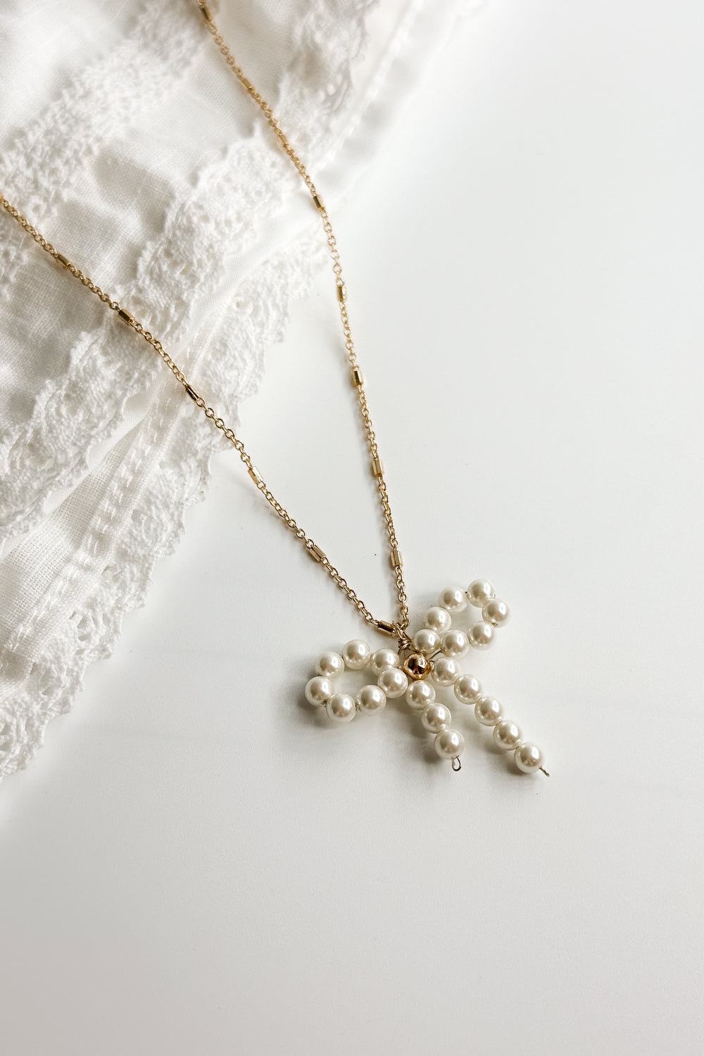 Close up view of the Mia Gold & Pearl Bow Necklace which features adjustable gold chain link with pearl bow attachment