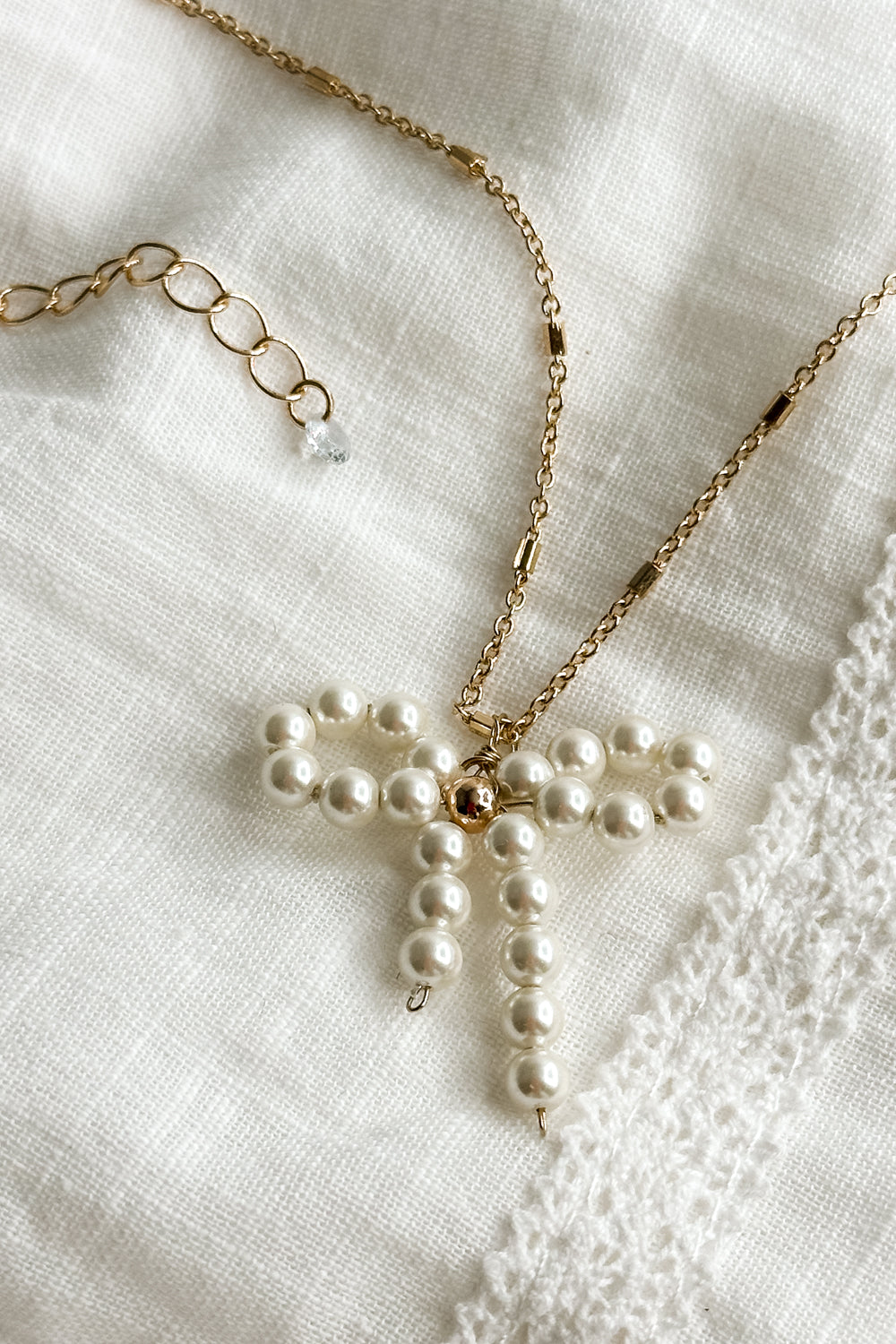 Close up view of the Mia Gold & Pearl Bow Necklace which features adjustable gold chain link with pearl bow attachment