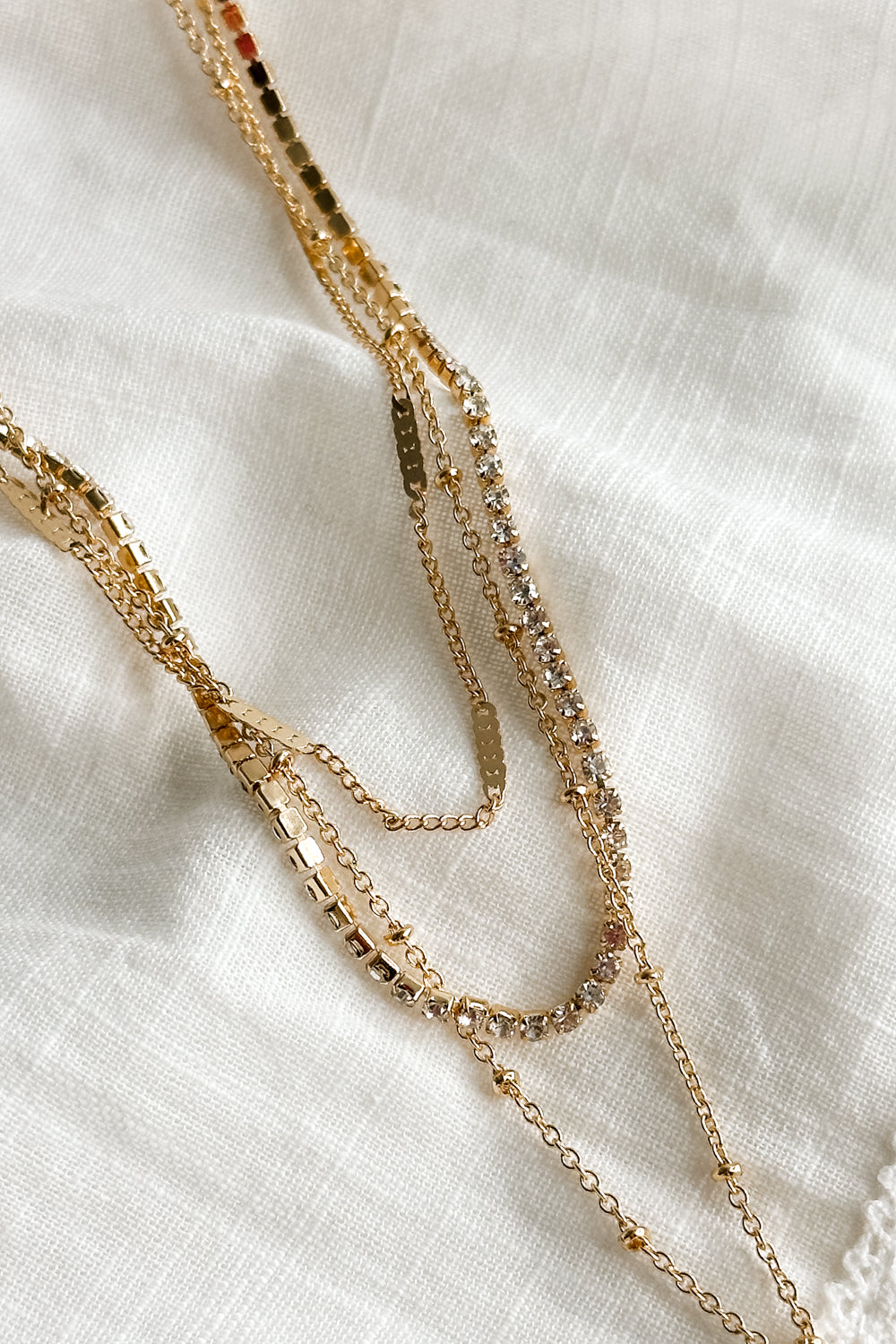 Close up view of the Celeste Gold Triple Layer Chain Heart Necklace which features two gold chain link layers, rhinestone layer, gold heart medallion and set in golds