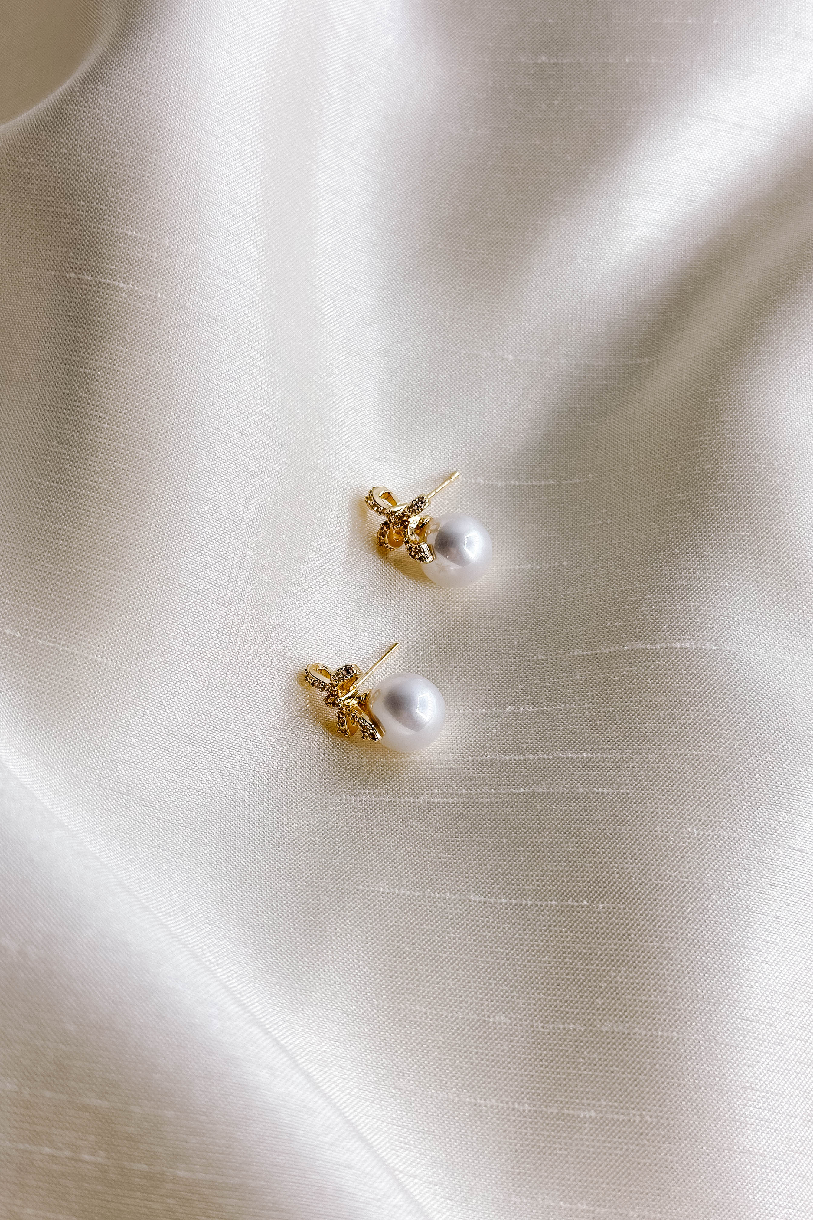 Flat lay close up view of both pearl earring with gold and rhinestone bow