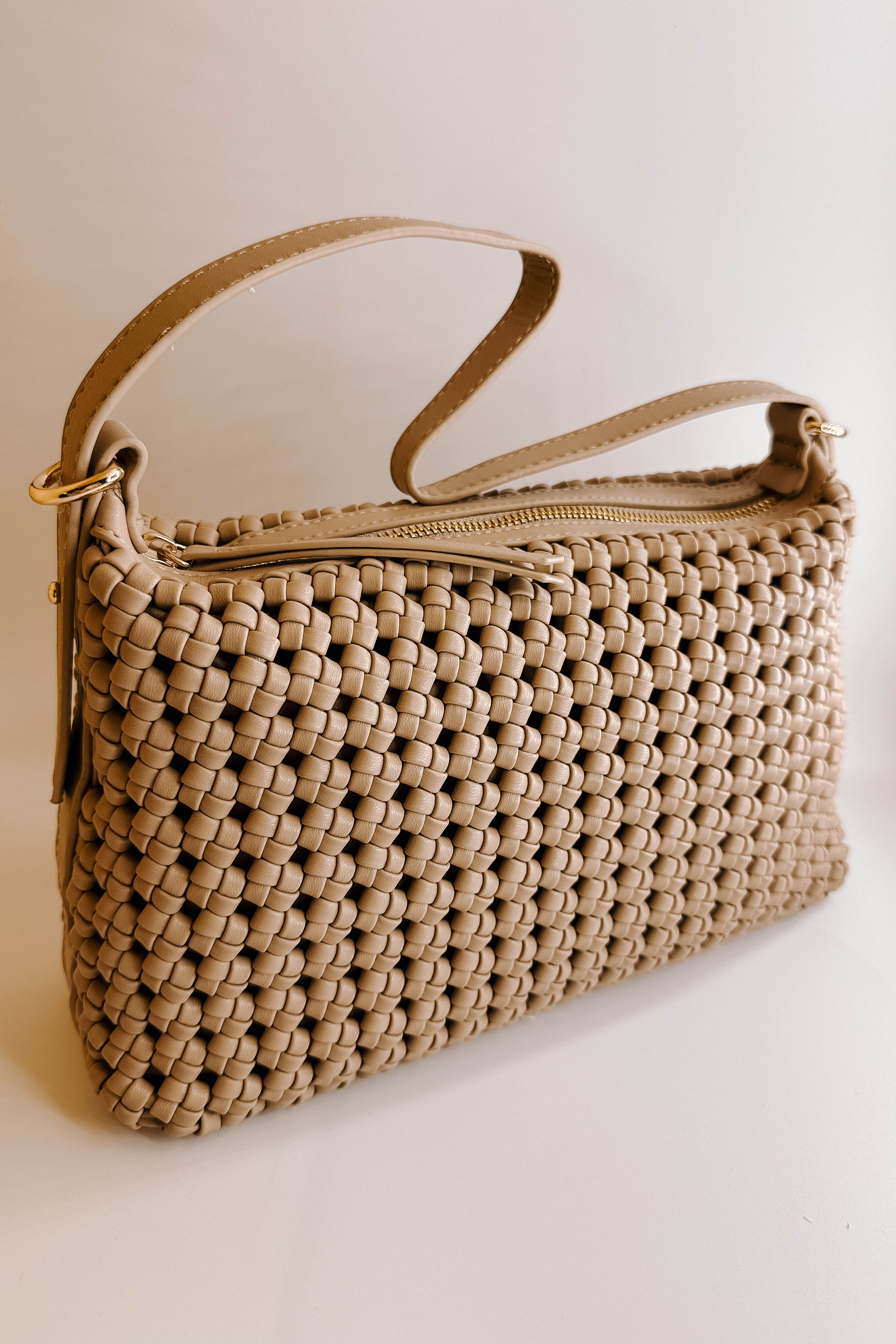 Front view of the Naya Beige Woven Purse against a white background.  It has dark beige faux-leather material with a woven design, short and long removable straps, gold hardware, and a patterned interior with a zippered pocket and a slit pocket.