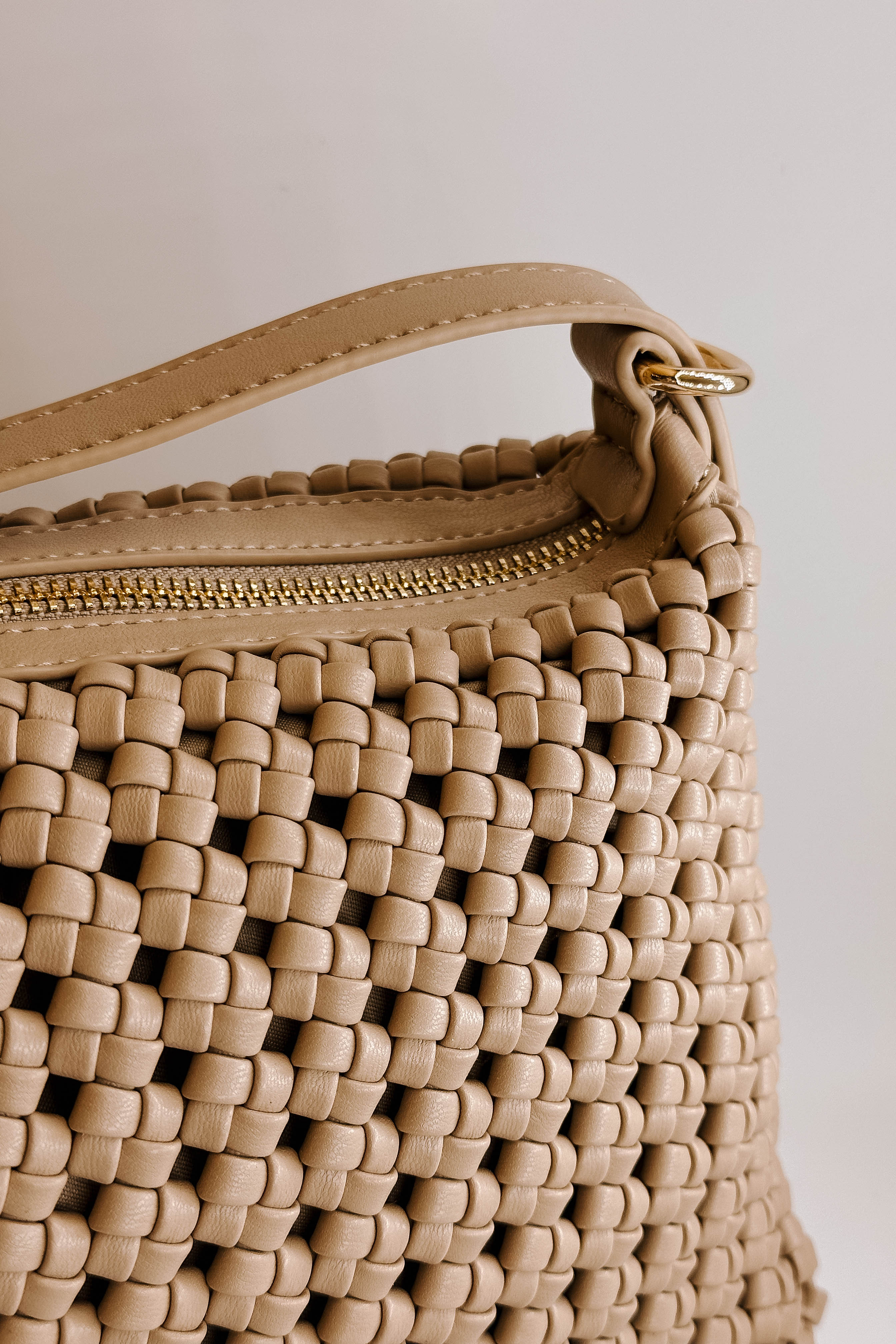 Close detailed front view of the Naya Beige Woven Purse.  It has dark beige faux-leather material with a woven design, short and long removable straps, gold hardware, and a patterned interior with a zippered pocket and a slit pocket.