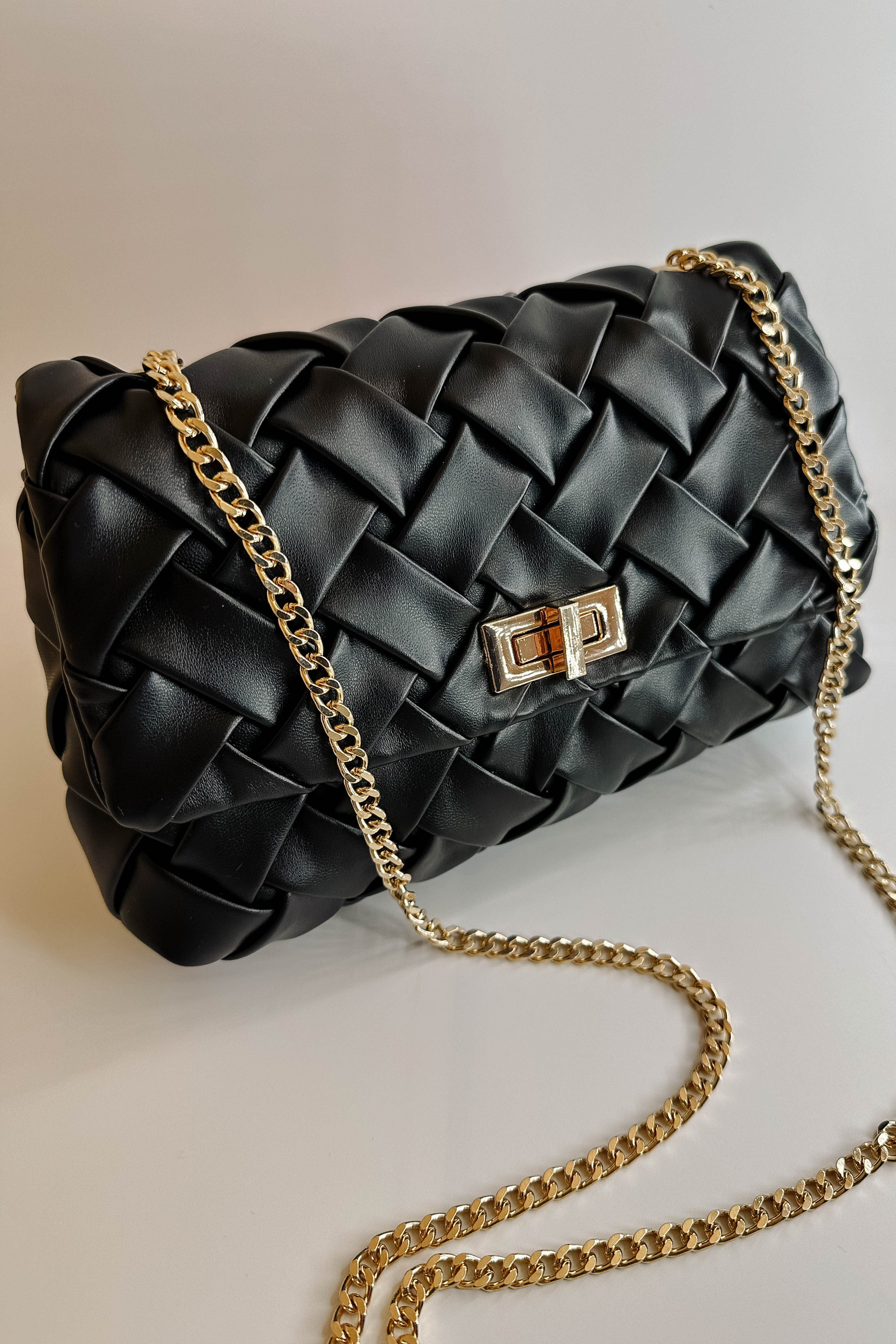 Front view of the Carrie Black Leather Woven Purse which features black woven leather fabric, gold button closure and gold chain link strap.