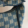 A close up zipper view of The Miley Denim Knot Handbag. This features a medium wash denim and tan pattern with a knot handle. There is a zipper closure along with a pocket on the inside.