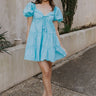 Full body view of female model wearing the  Gloria Light Blue Short Sleeve Mini Dress which features aqua blue cotton fabric, aqua blue lining, mini length, ruffle tiered details, a sweetheart neckline with drawstring ties, a smocked back, and short puff sleeves.