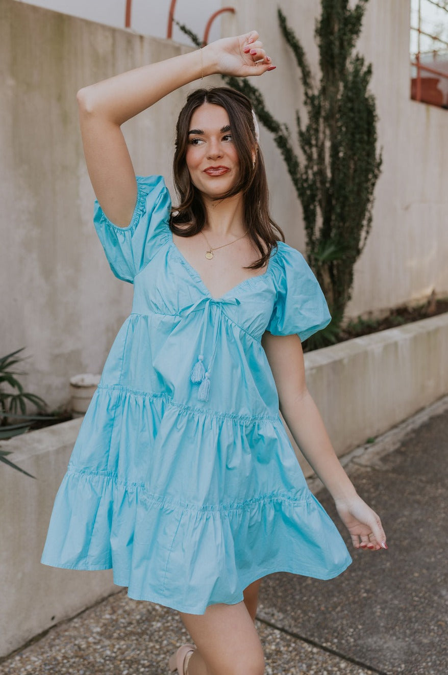 Front view of female model wearing the Gloria Light Blue Short Sleeve Mini Dress which features aqua blue cotton fabric, aqua blue lining, mini length, ruffle tiered details, a sweetheart neckline with drawstring ties, a smocked back, and short puff sleeves.