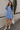 Full body view of model wearing the Nicole Blue Ruffle Short Sleeve Mini Dress which features chambray blue light weight fabric, mini length, chambray blue lining, two-tiered design, two side pockets, square neckline and ruffle short sleeves.