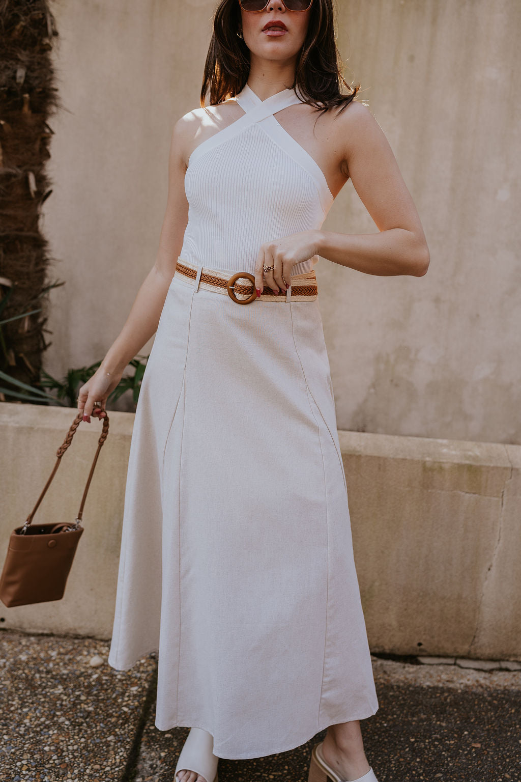 Front view of model wearing the Seychelles Linen Midi Skirt which features natural linen fabric, midi length, flared skirt, natural lining, belt loops, brown and natural crochet adjustable belt and monochrome side zipper with hook closure.