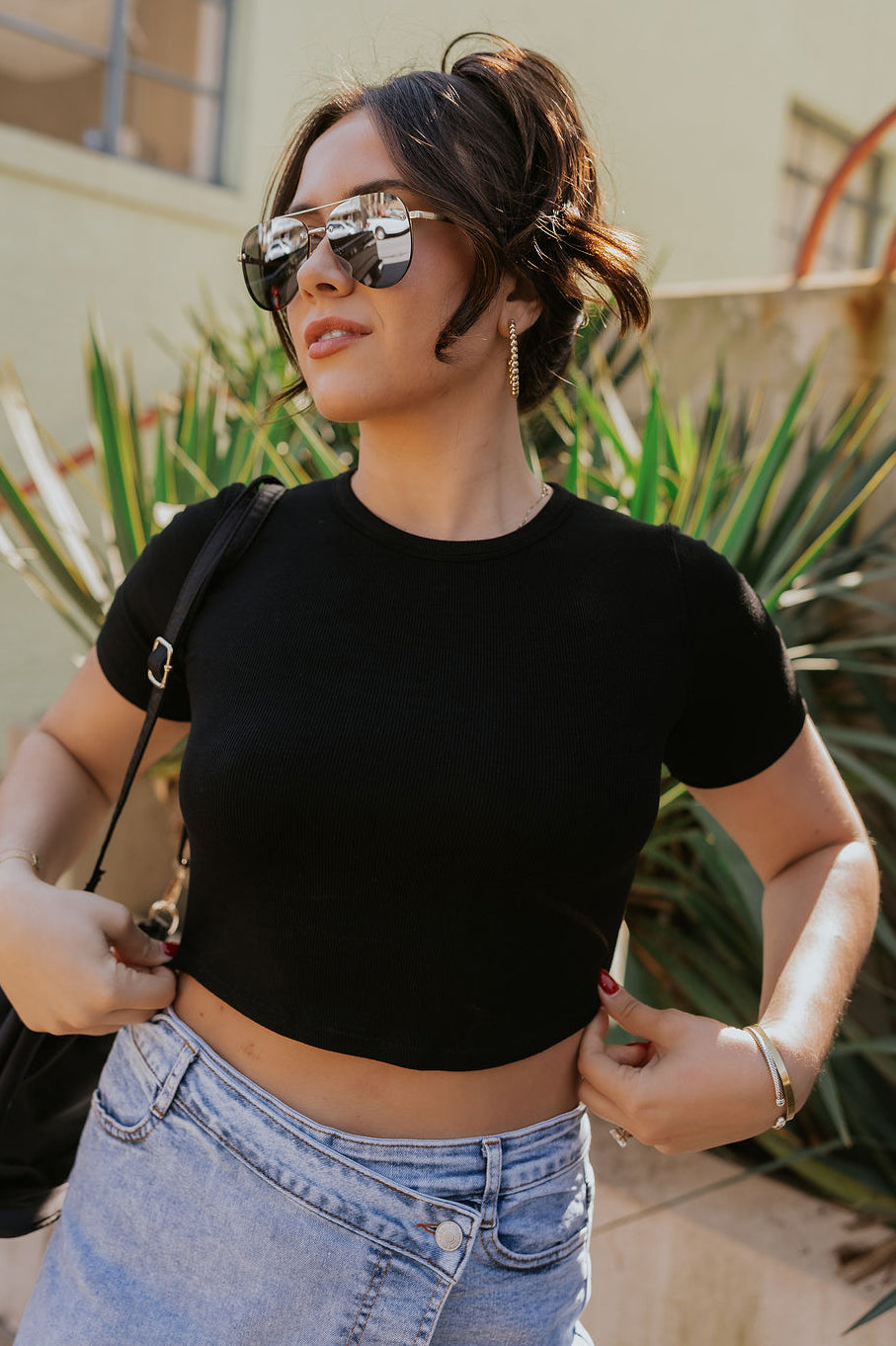 Front view of model wearing the Lucy Black Cropped Short Sleeve Top which features black ribbed knit fabric, cropped waist, round neckline and short sleeves.