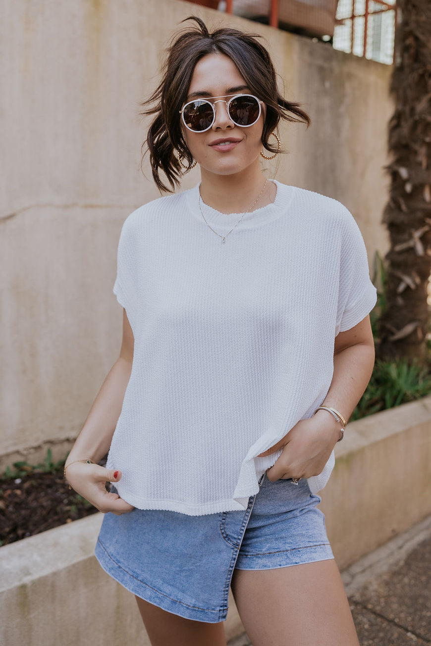 Front view of model wearing the Everly Off White Ribbed Short Sleeve Top which features white ribbed fabric, a round neckline, and short dolman sleeves with ribbed cuff details.