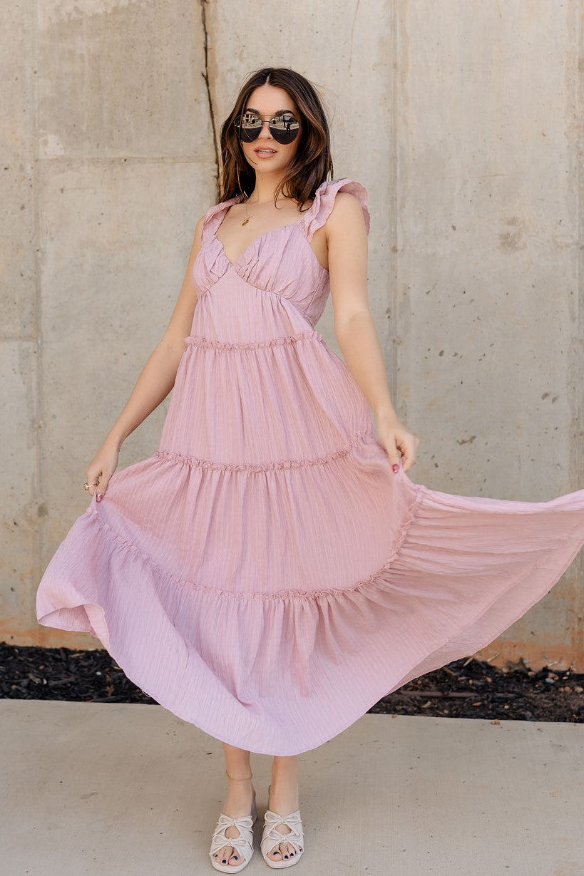 Full body front view of model wearing the Santorini Blush Maxi Dress that features textured blush fabric, maxi length, blush lining, tiered ruffle hem details, a sweetheart neckline, and ruffle straps.