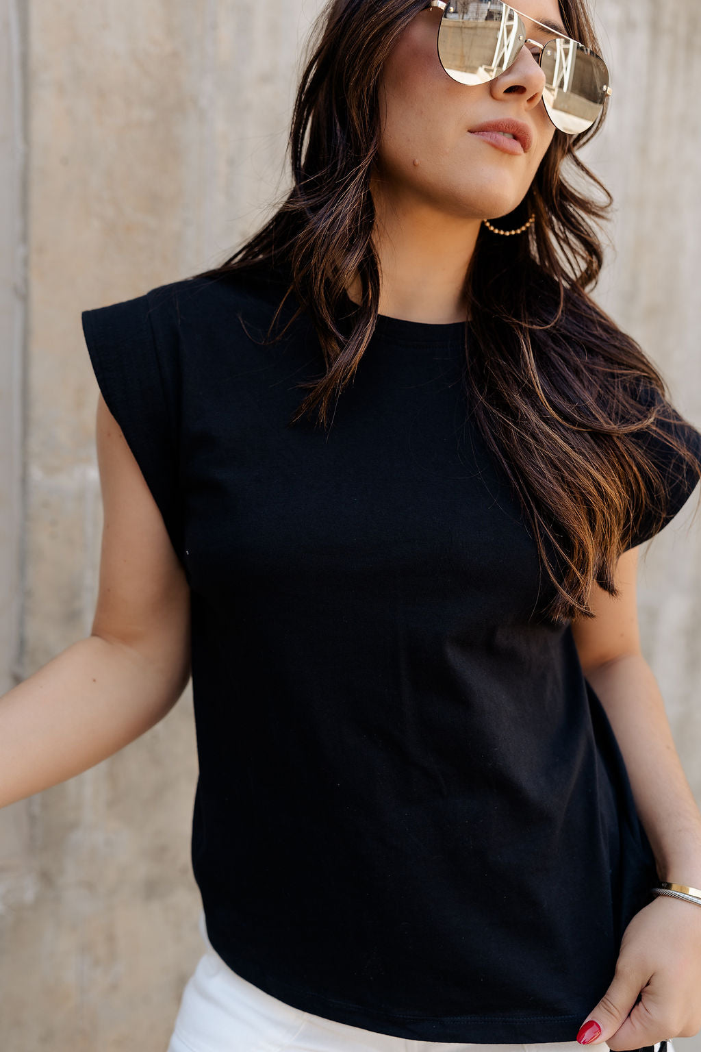 Close-up front view of model wearing the Iris Black Sleeveless Top that features black cotton fabric, a round neckline, and short sleeves with stitched ribbed hem details.