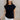Front view of model wearing the Iris Black Sleeveless Top that features black cotton fabric, a round neckline, and short sleeves with stitched ribbed hem details.