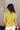 Back view of model wearing the Iris Chartreuse Sleeveless Top which features chartreuse cotton fabric, round neckline and short sleeves with stitch detail hem.