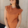 Front view of model wearing the Rylee Rust Sleeveless Top which features rust brown knit fabric, round neckline and sleeveless with gold stud details.