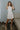 Full body front view of model wearing the cream colored Eleanor Sleeveless Button Front Mini Dress that has cotton fabric, a button-up front with silver buttons, buttoned chest pockets, a collared neckline, and a racerback cut.