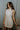 Front view of model wearing the cream colored Eleanor Sleeveless Button Front Mini Dress that has cotton fabric, a button-up front with silver buttons, buttoned chest pockets, a collared neckline, and a racerback cut.