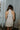 Back view of model wearing the cream colored Eleanor Sleeveless Button Front Mini Dress that has cotton fabric, a button-up front with silver buttons, buttoned chest pockets, a collared neckline, and a racerback cut.