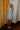 Full body back view of model wearing the blue colored Eleanor Sleeveless Button Front Mini Dress that has cotton fabric, a button-up front with silver buttons, buttoned chest pockets, a collared neckline, and a racerback cut.