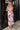 Full body view of model wearing the Isla Multi Swirl Midi Dress which features purple, fuchsia, peach, yellow, green, light pink and white knit fabric, wattercolor swirl print, peach lining, mid length, v-neckline, thick straps and sleeveless.