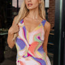 Front view of model wearing the Isla Multi Swirl Midi Dress which features purple, fuchsia, peach, yellow, green, light pink and white knit fabric, wattercolor swirl print, peach lining, mid length, v-neckline, thick straps and sleeveless.