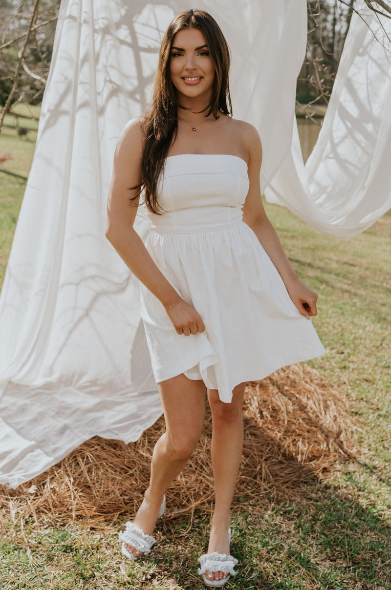 Full body view of female model wearing the Abigail Strapless Flare Mini Dress in white which features features Mini Length, Lining, Two Side Pockets, Strapless and Monochrome Back Zipper with Hook Closure.