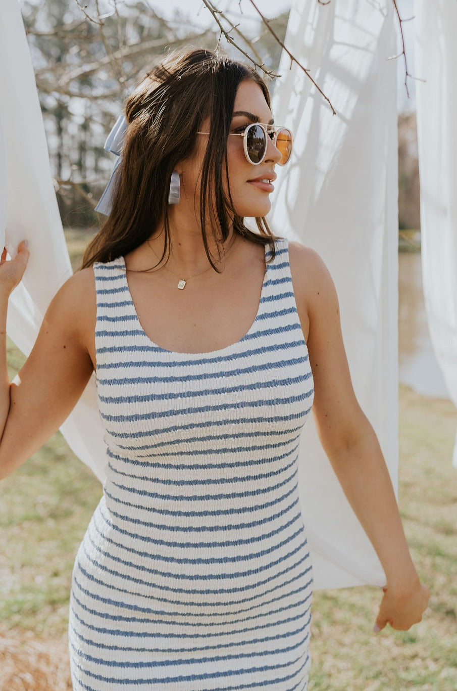 Upper body front view of female model wearing the Casey Cream & Blue Striped Midi Dress that has cream and blue horizontal stripes, bodycon fit, thick straps, a side slit, and round neck.