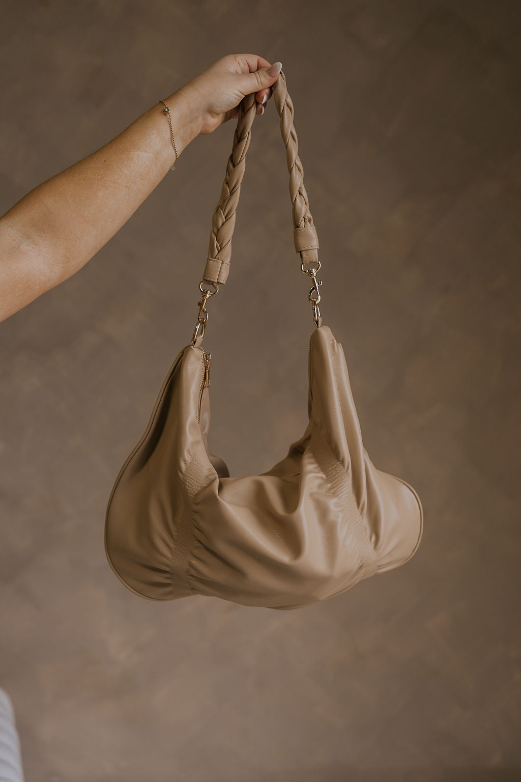 Front view of female model holding the Amber Natural Braided Purse which features natural tan leather fabric, braided strap, gold zipper and gold hardware details