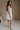 Full body side view of female model wearing the Kate Off White Floral Strapless Mini Dress which features White Floral Print, Tiered Body, Mini Length, White Lining Sweetheart Neckline, Strapless and Back Zipper with Hook Closure.
