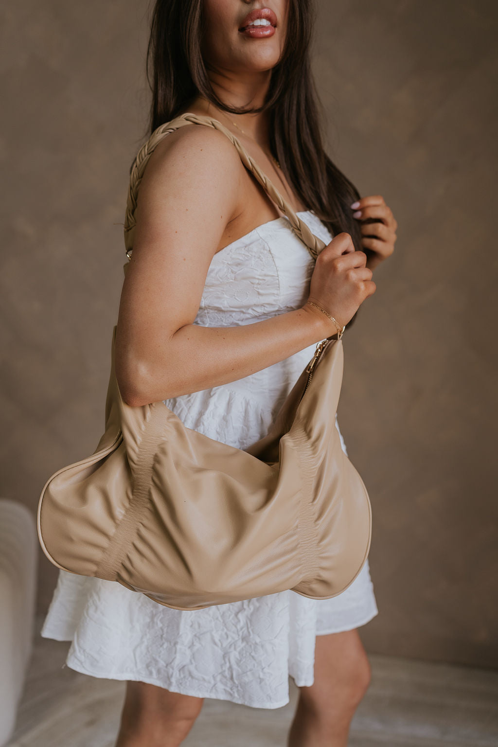 Close up side view of female model wearing the Amber Natural Braided Purse which features natural tan leather fabric, braided strap, gold zipper and gold hardware details