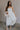 Full body view of female model wearing the Rebecca Off White Pearl Bow Midi Dress which featuresCream Sheer Fabric, Midi Length, Cream Lining, Strapless, Pearl Details and Bow Back Detail