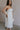Side view of female model wearing the Rebecca Off White Pearl Bow Midi Dress which featuresCream Sheer Fabric, Midi Length, Cream Lining, Strapless, Pearl Details and Bow Back Detail