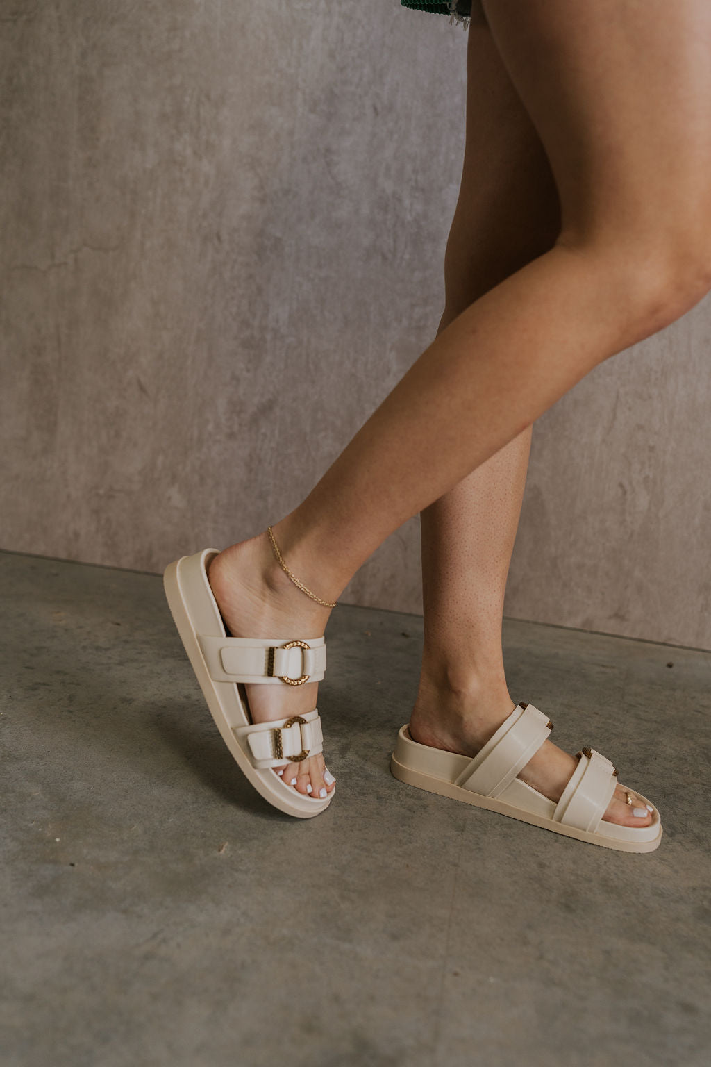 Right side view of female model wearing the Soya Sandal in White Leather which features white leather fabric, chunky sole, gold hammered metallic ring accents and slip-on style