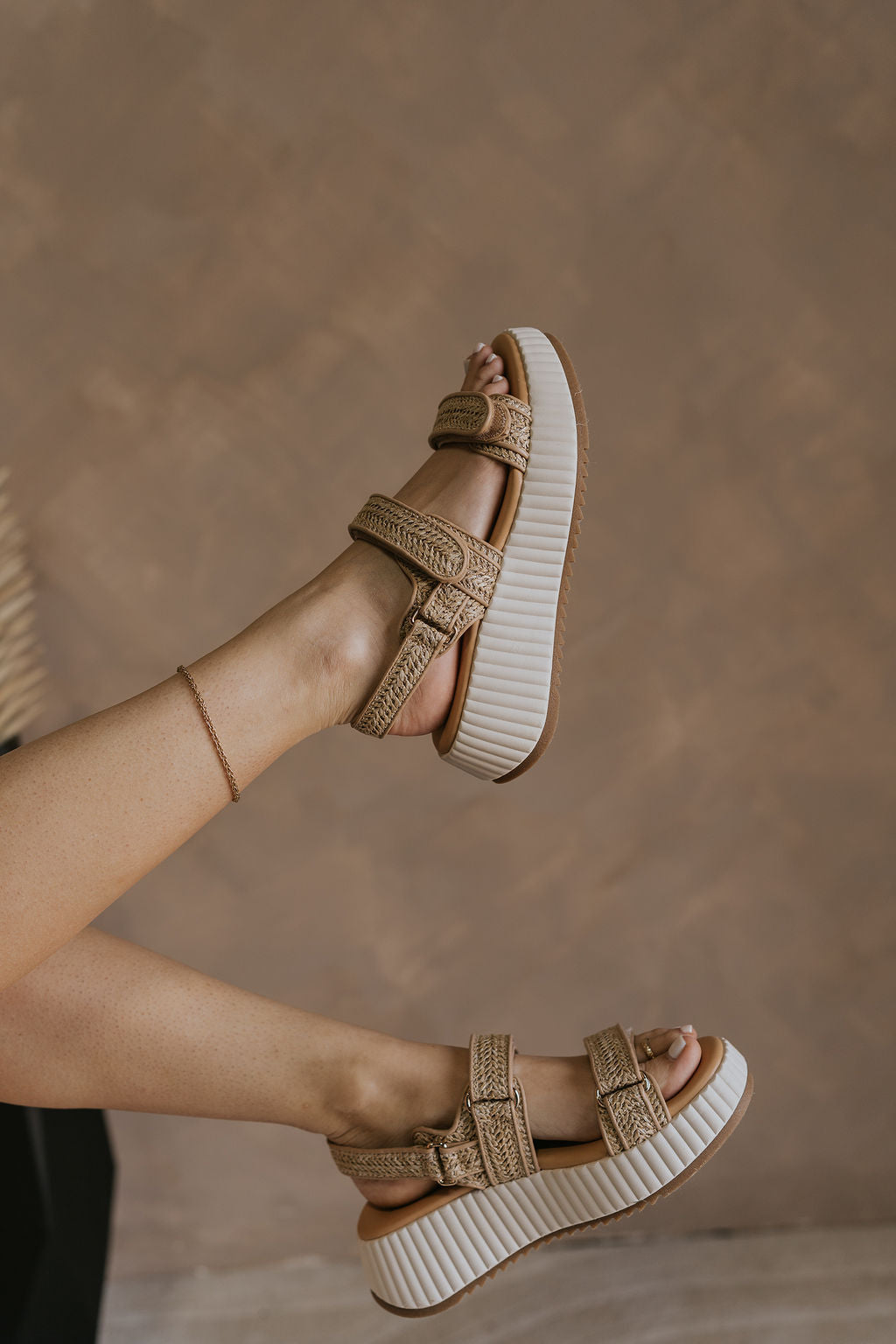 Right side view of female model wearing the Fighter Sandal in Natural which features natural tan texture fabric, rattan details, white platform sole and adjustable velcro straps