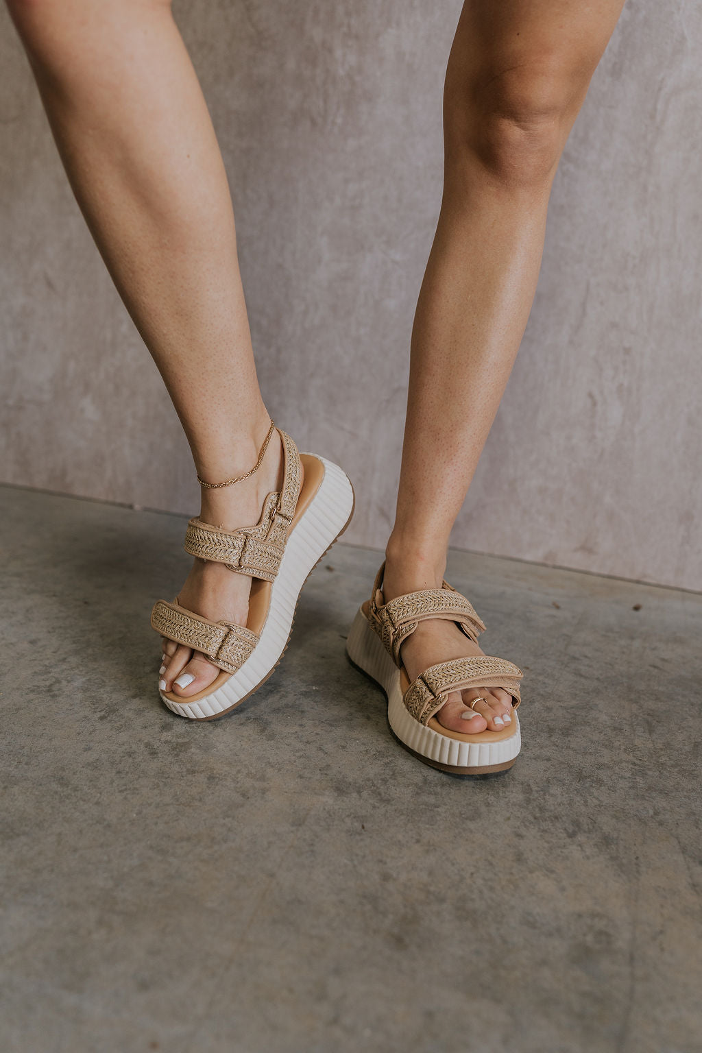 Front view of female model wearing the Fighter Sandal in Natural which features natural tan texture fabric, rattan details, white platform sole and adjustable velcro straps
